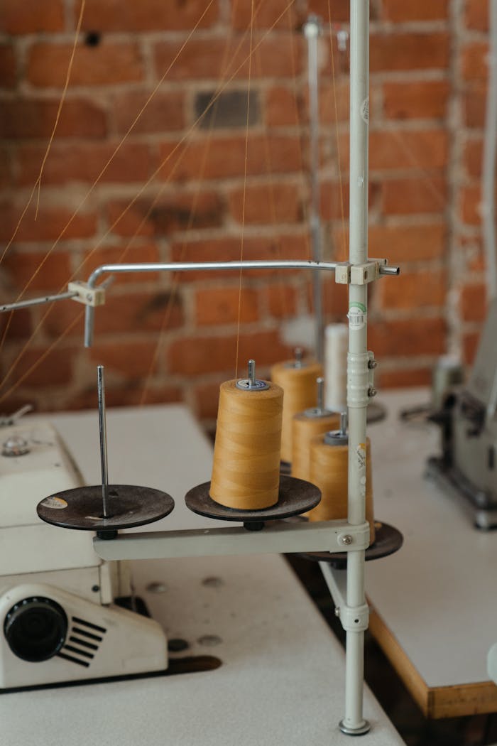 Close-up of thread spools on an industrial sewing machine against a brick wall backdrop.