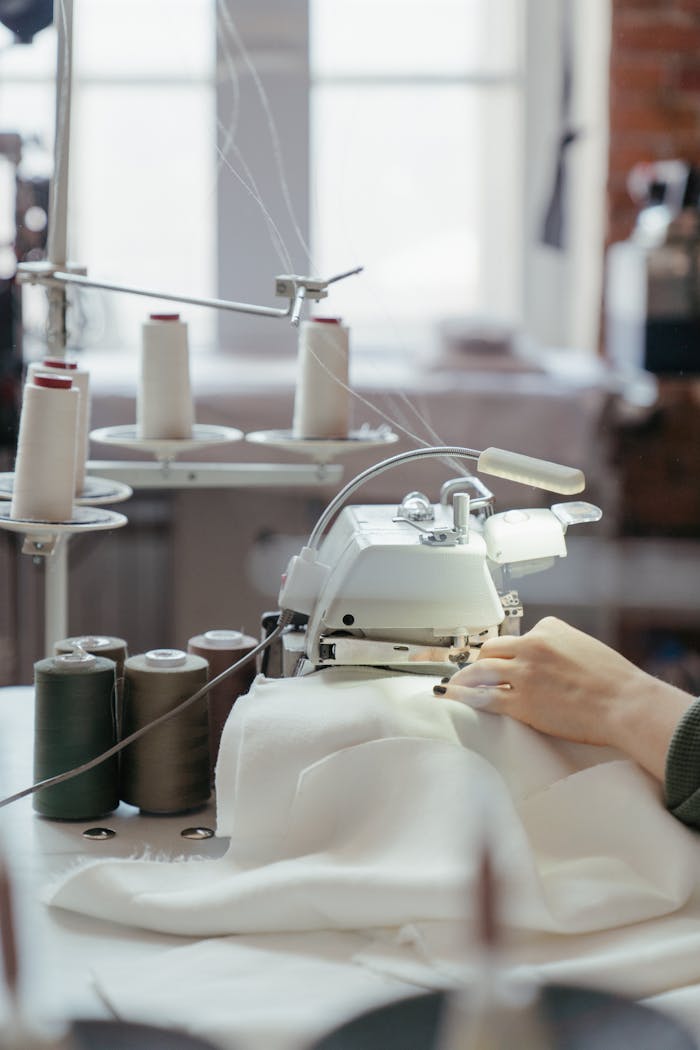 services-04 A person sewing fabric on a professional machine in a well-lit workshop with spools of thread.
