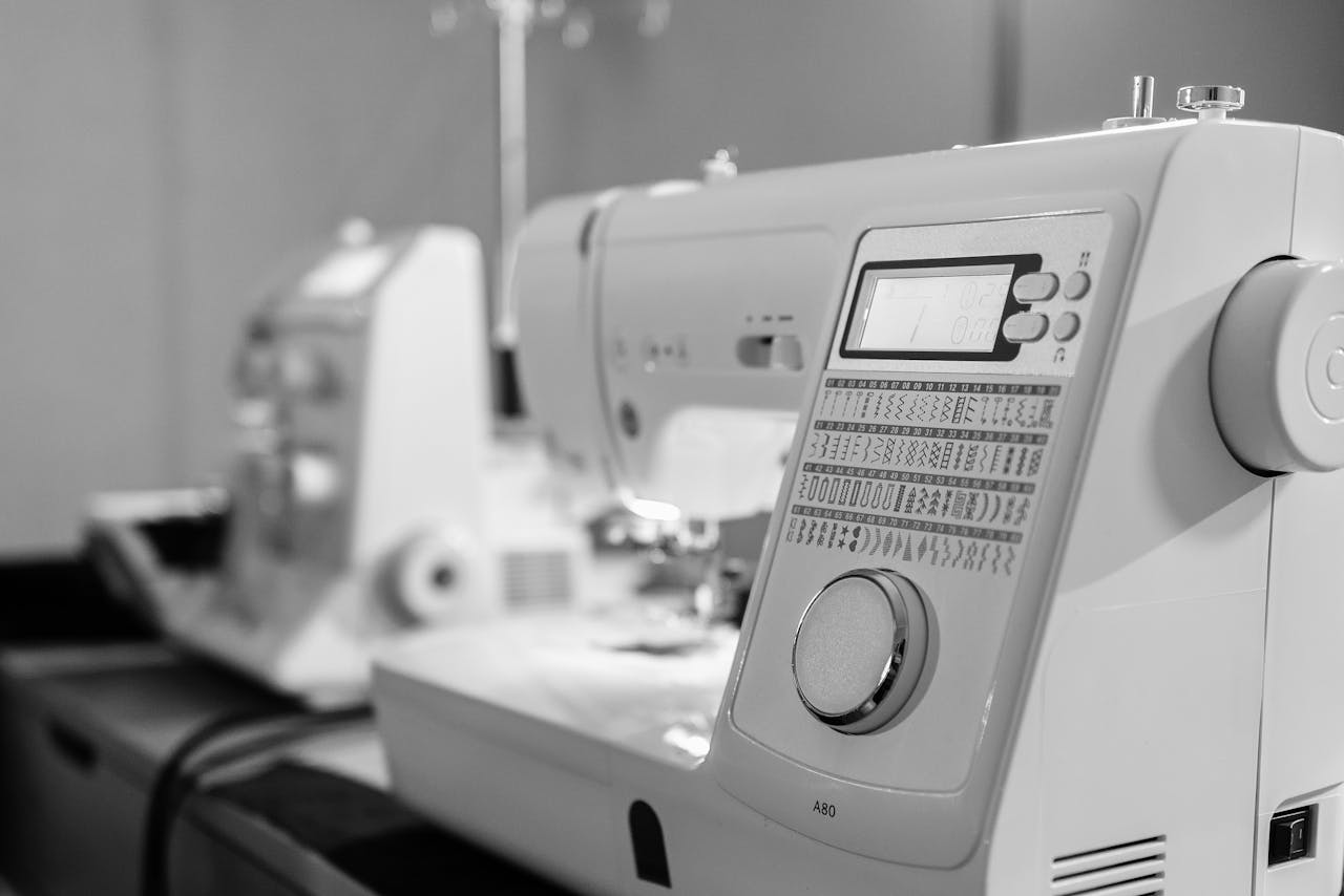 who-we-are A detailed black and white close-up of a modern sewing machine showcasing its digital controls and patterns.